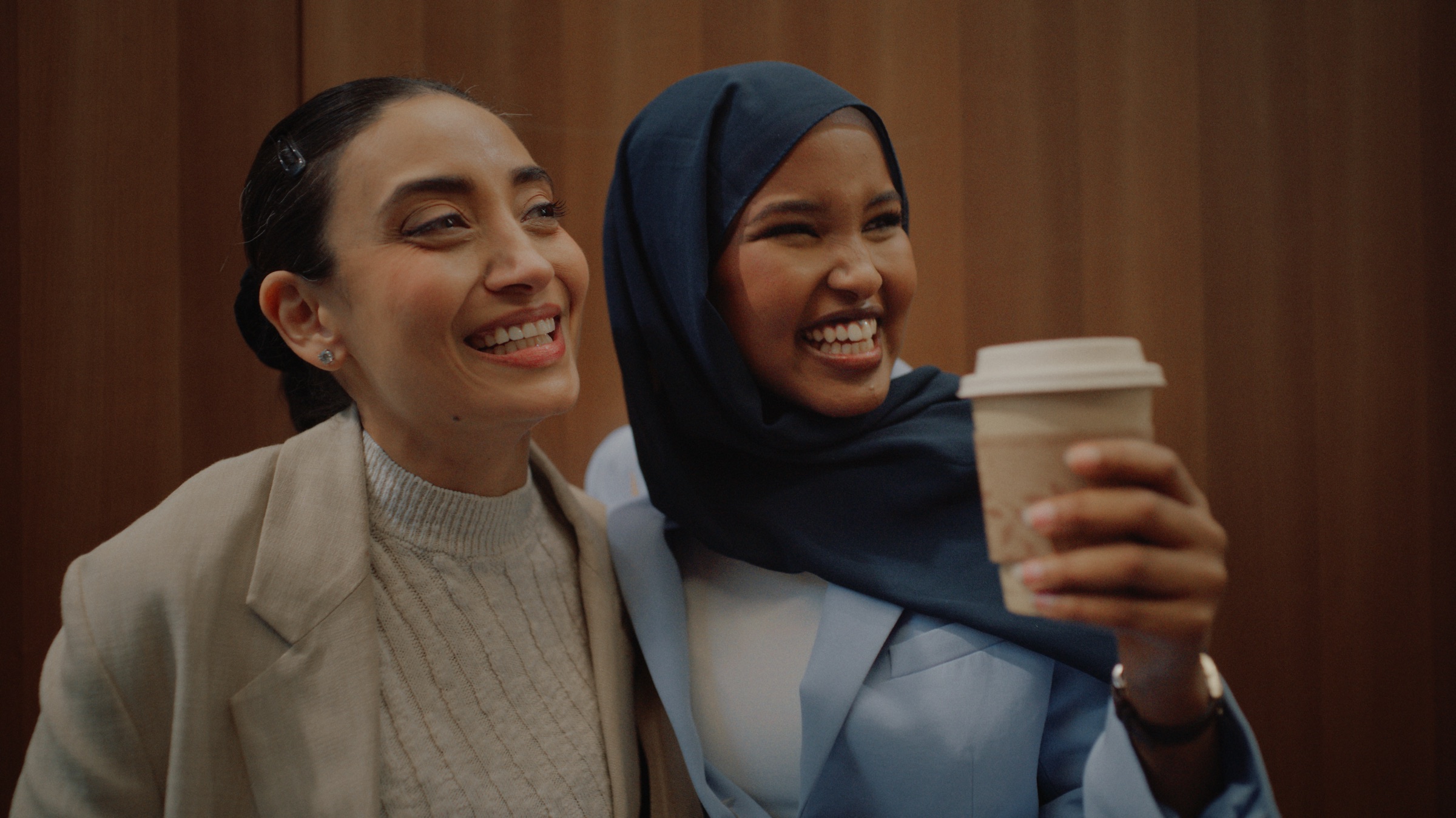 Two women laughing together, one holding a coffee cup.